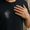 漂白剤で白くシミになった黒いTシャツと驚いた表情の人物の手元