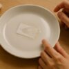 シール跡が残った白い陶器の皿と、対処法に悩む手元のイメージカット